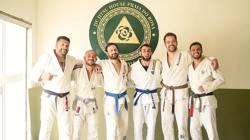 Turma reunida de kimono diante do selo da Jiu-Jitsu House Praia do Rosa.