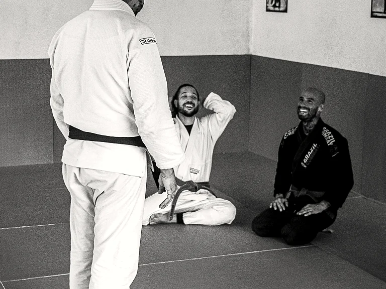 Treino de técnica no tatame, com alunos acompanhando.