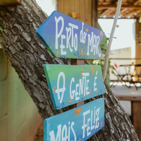 Placas de madeira pintadas à mão penduradas numa árvore: perto do mar a gente é mais feliz.