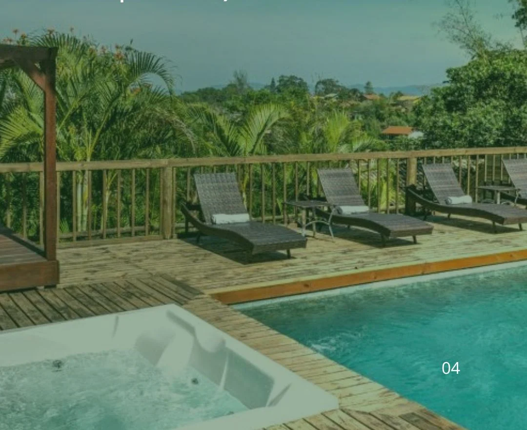 Deck de madeira da pousada com espreguiçadeiras, piscina e a mata da Praia do Rosa ao fundo.