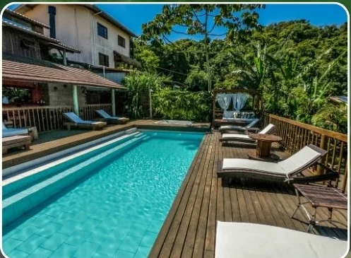 Piscina da pousada com deck de madeira, espreguiçadeiras e mata ao redor.