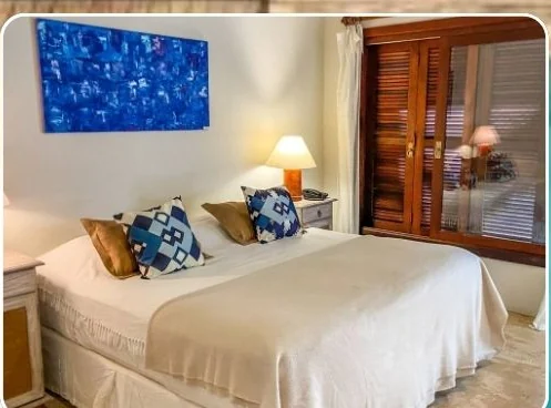 Quarto da pousada com cama de casal arrumada e janela de madeira.