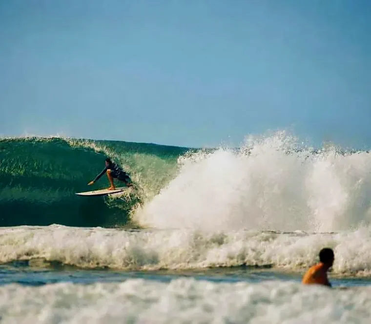 Surfista fazendo um drop na parede de uma onda limpa na Praia do Rosa, com a espuma explodindo ao lado.