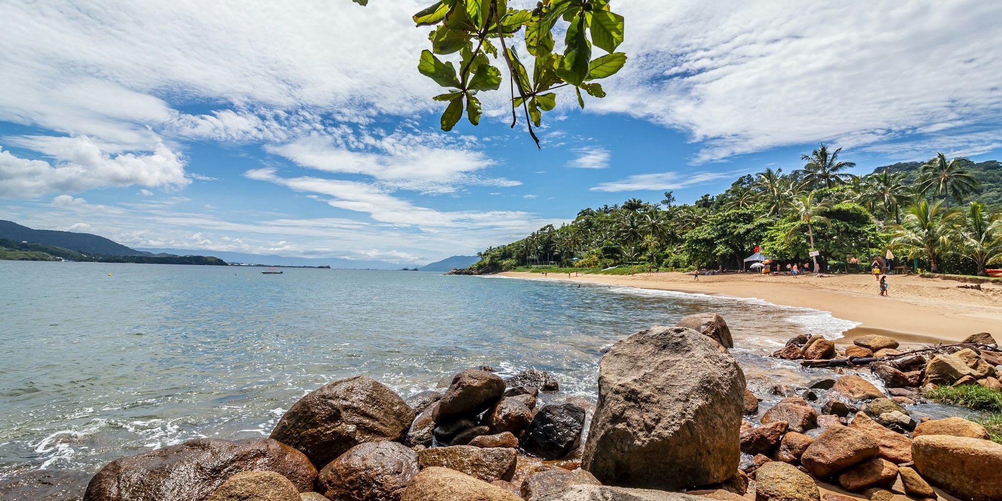 Praia de Ilha Bela com pedras na areia, coqueiros e a mata descendo até o mar.