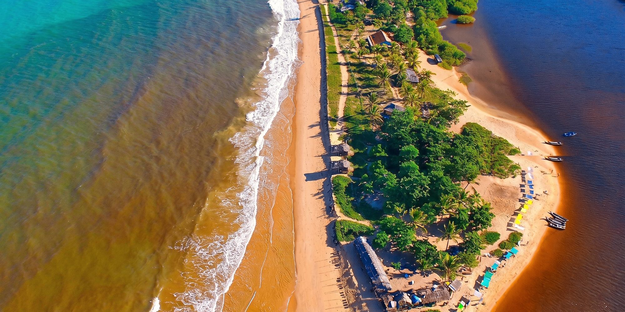 Vista do alto da praia de Caraíva, onde o rio encontra o mar, entre coqueiros.