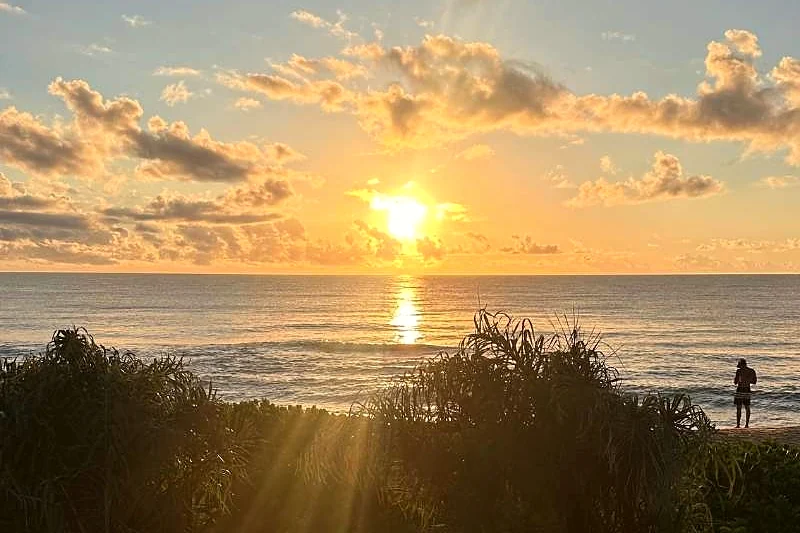 Pôr do sol sobre o mar visto da restinga, com pessoas ao longe.