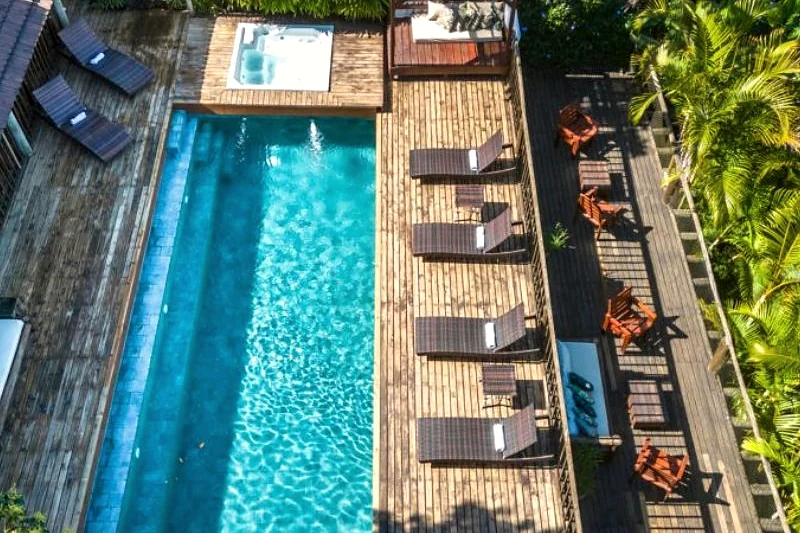 Vista aérea da piscina e do deck de madeira da casa, entre a vegetação.