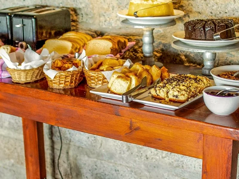 Mesa de café da manhã com pães, bolos e frutas.