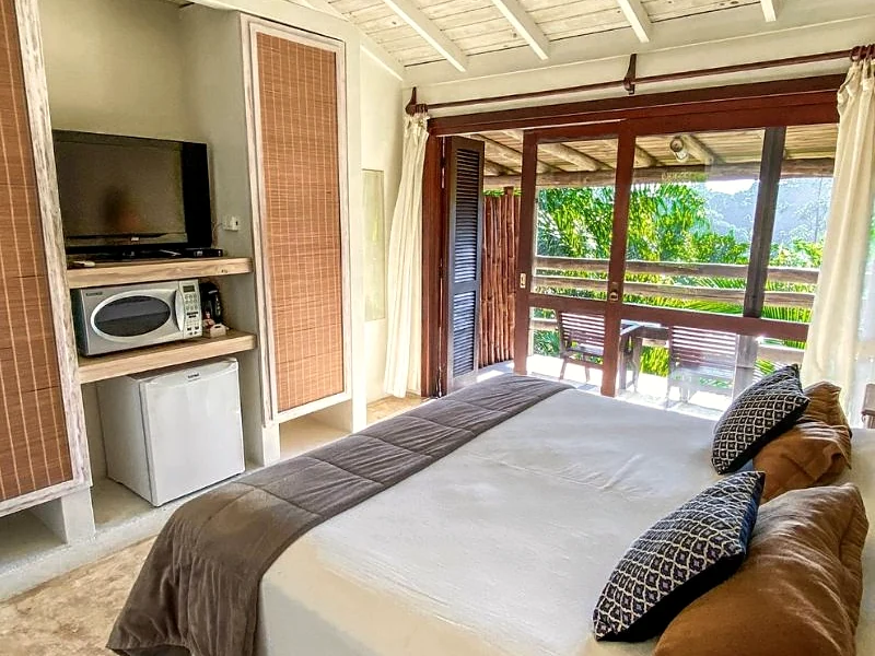 Quarto com cama arrumada e porta aberta para a varanda.