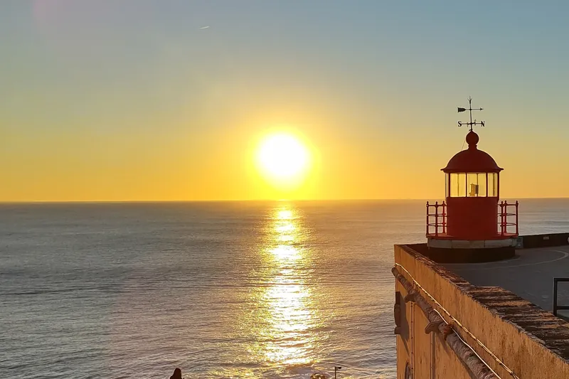 Pôr do sol no mar visto do farol, com a lanterna vermelha no canto.