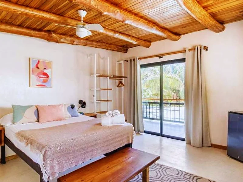 Quarto de madeira com cama de casal e porta para a varanda.