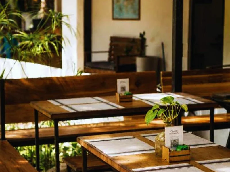 Área de refeições do hotel com mesas de madeira e plantas.