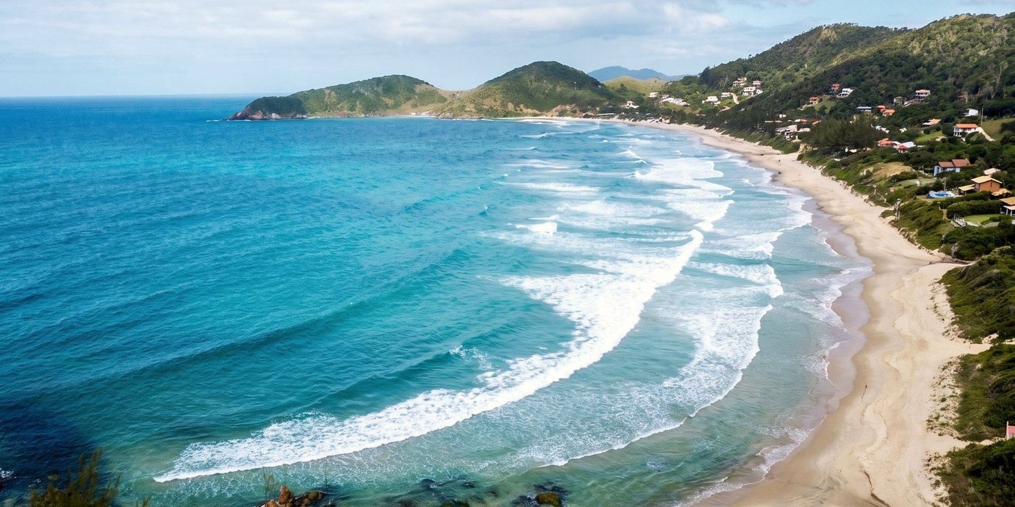 Vista aérea da enseada da Praia do Rosa, com a praia aberta e os morros cobertos de mata.