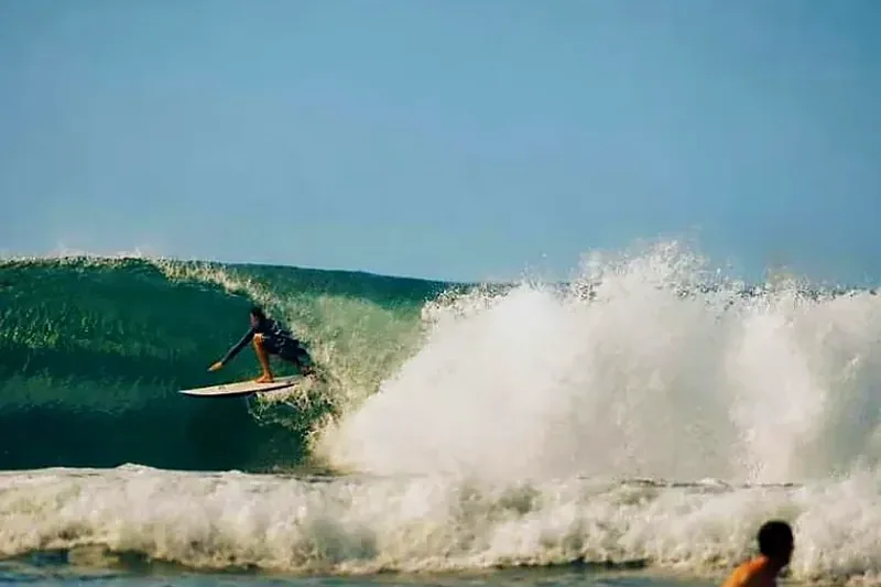 Surfista fazendo um drop na parede de uma onda limpa na Praia do Rosa, com a espuma explodindo ao lado.