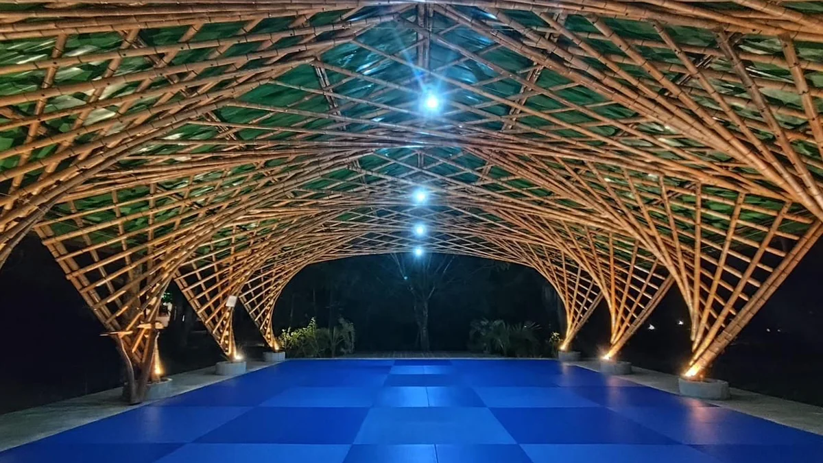 O Coliseo à noite: tatame azul sob a abóbada de bambu, com iluminação cênica entre os arcos.