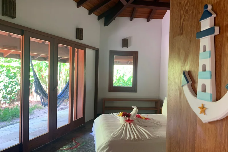 Quarto da suíte com cama de casal e portas de madeira abertas para a varanda com rede.
