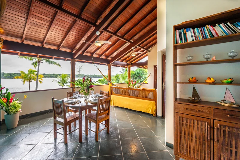 Sala de jantar aberta para o jardim, com mesa posta e vista para os coqueiros e o mar.